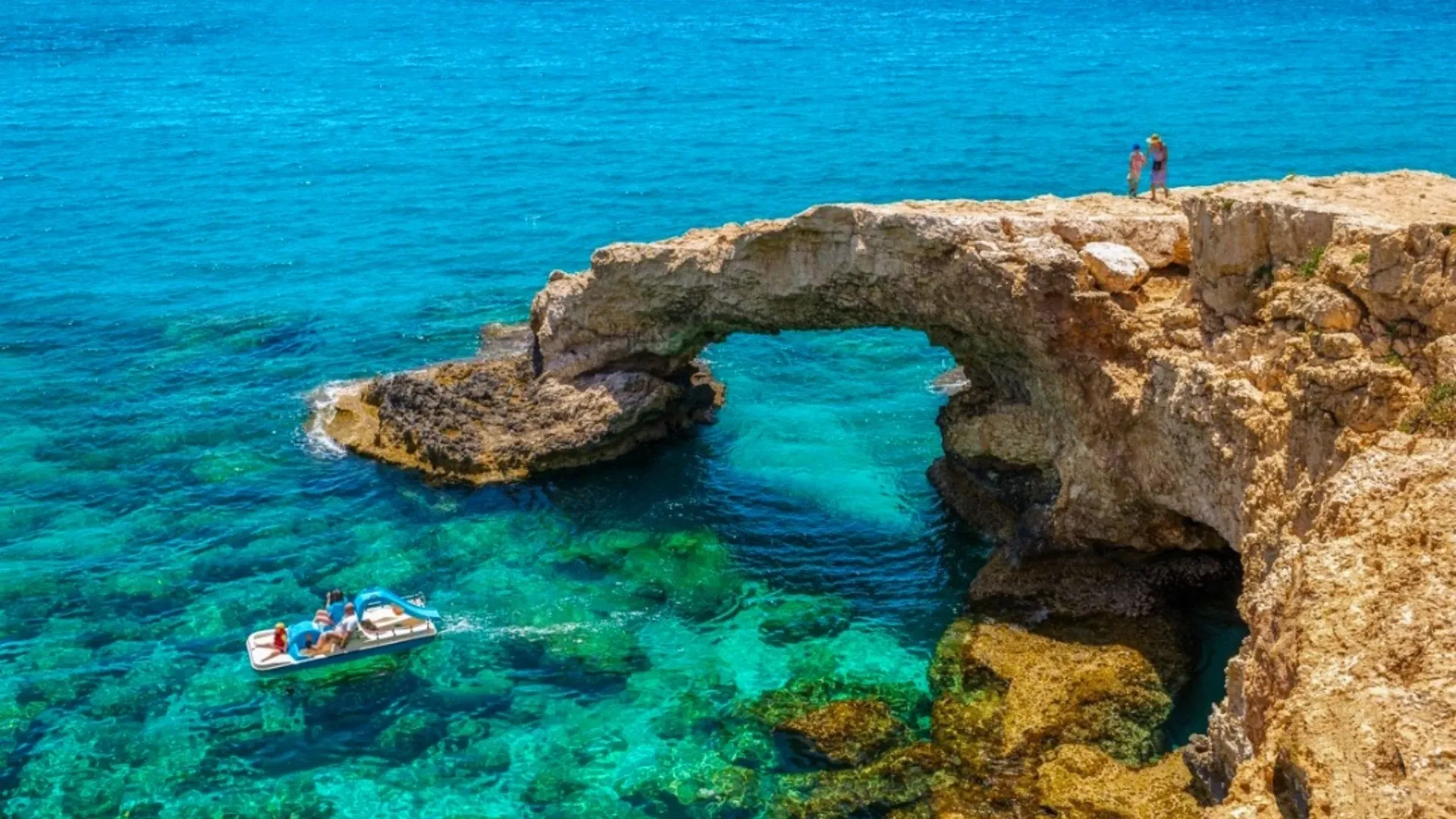 סירה קטנה מפליגה במים צלולים ליד גשר סלע טבעי